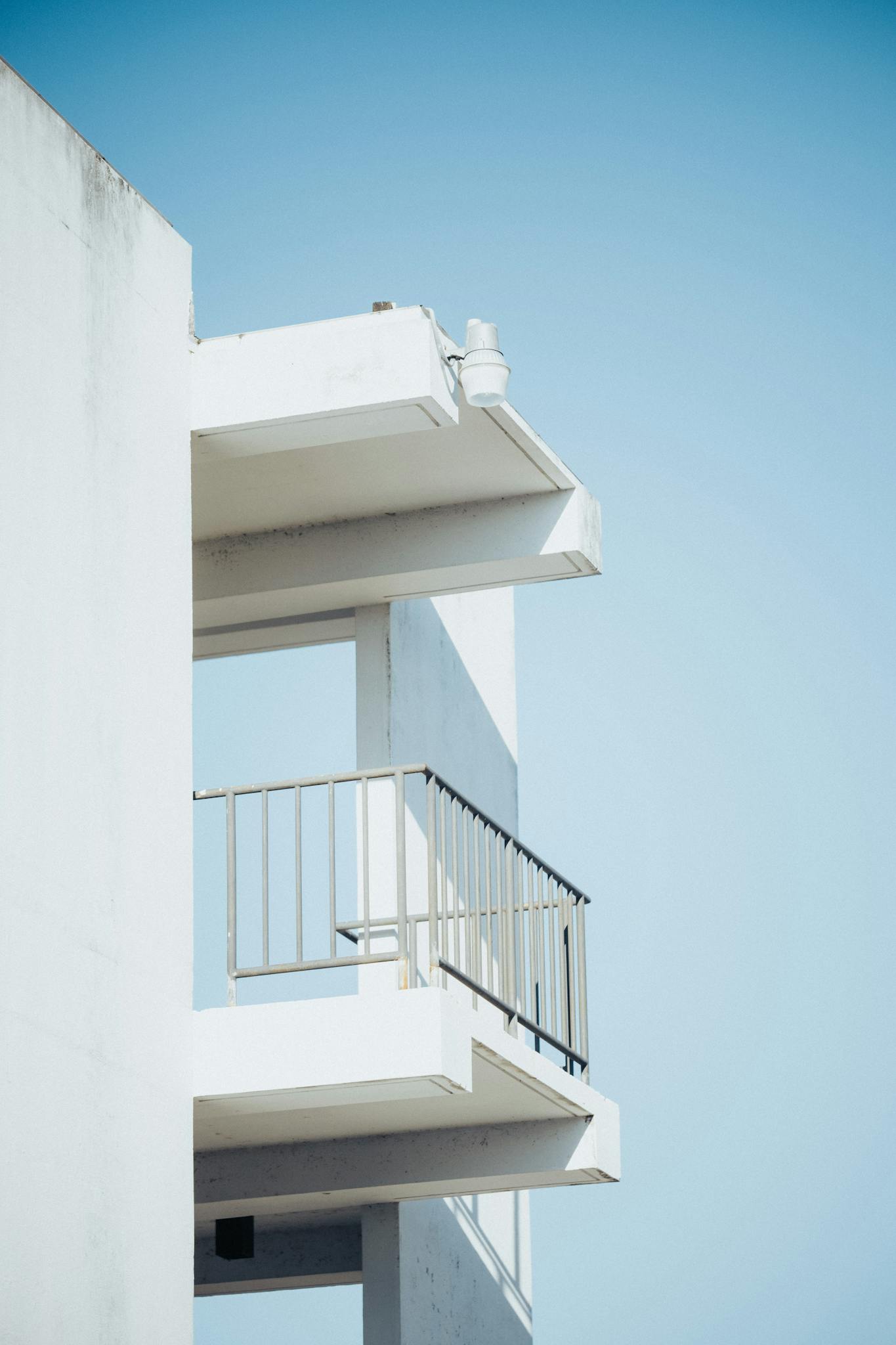 Minimalist view of a modern building's balcony against a bright blue sky.