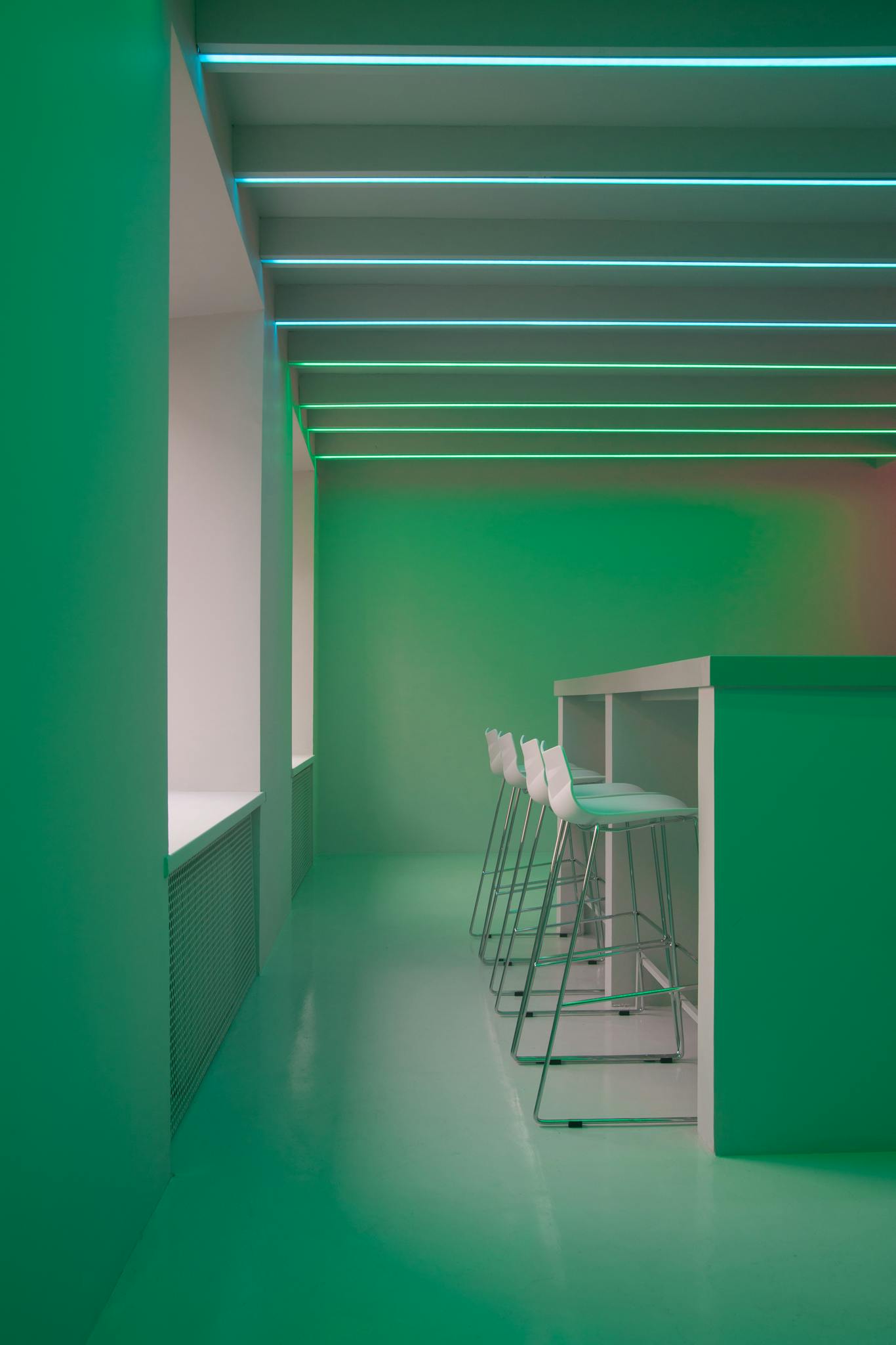 A minimalist green interior featuring modern design with sleek stools and innovative lighting.