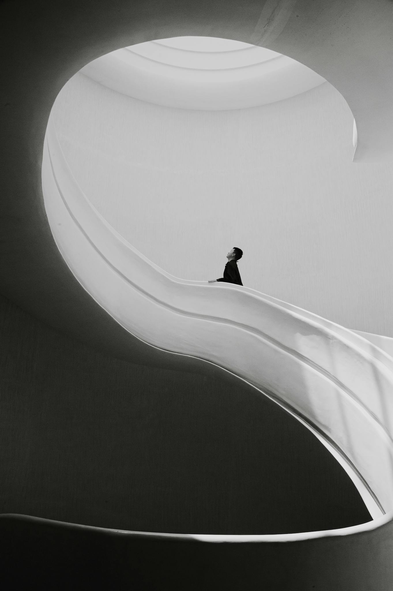 Minimalist black and white photograph of a person on a modern spiral staircase.